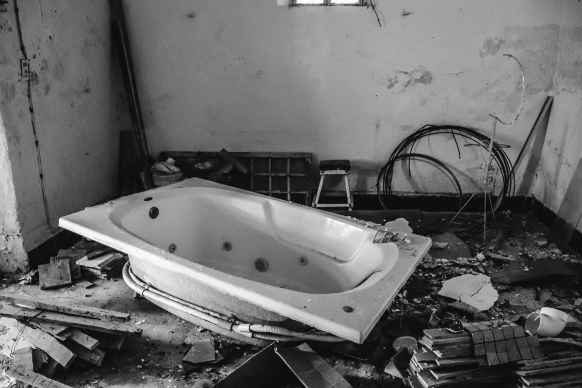 Bathtub pulled out during a bathroom strip-out, broken tile and debris across the floor