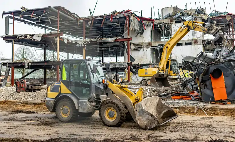 Loader and excavator clearing a partly demolished building down to its frame