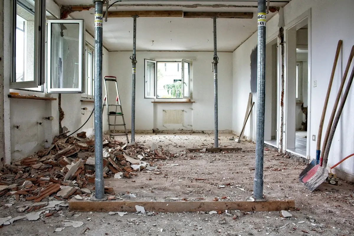 Interior wall removed and held with temporary steel props during a strip-out, rubble across the floor