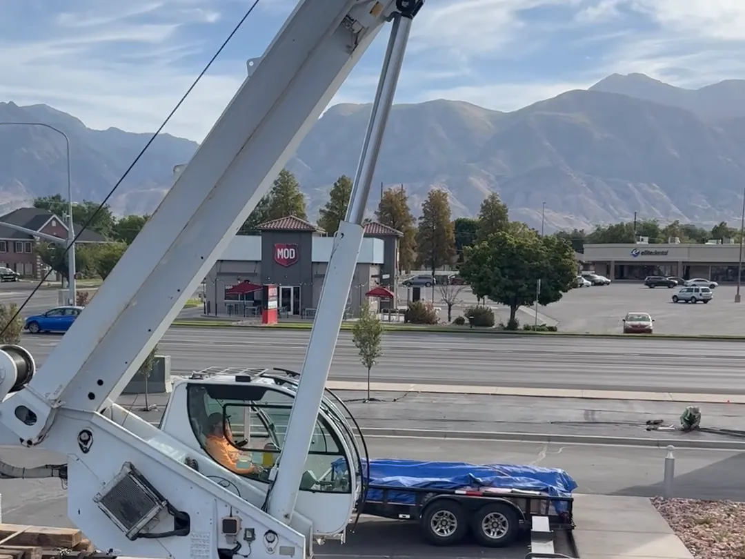 Crane truck set up beside a commercial building with the mountains in the background