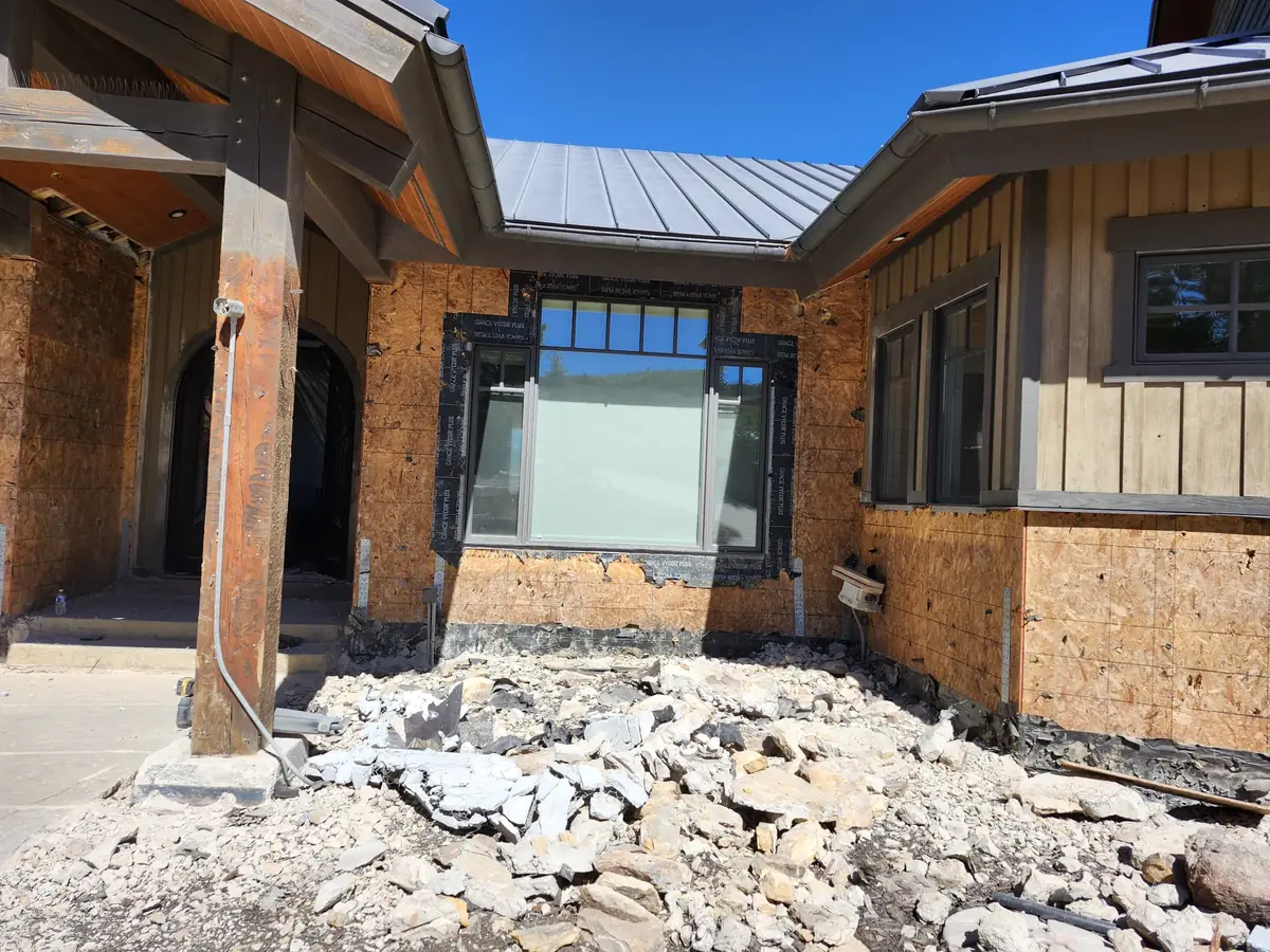 House exterior with the stone veneer torn off down to the sheathing and broken stone piled at the entry