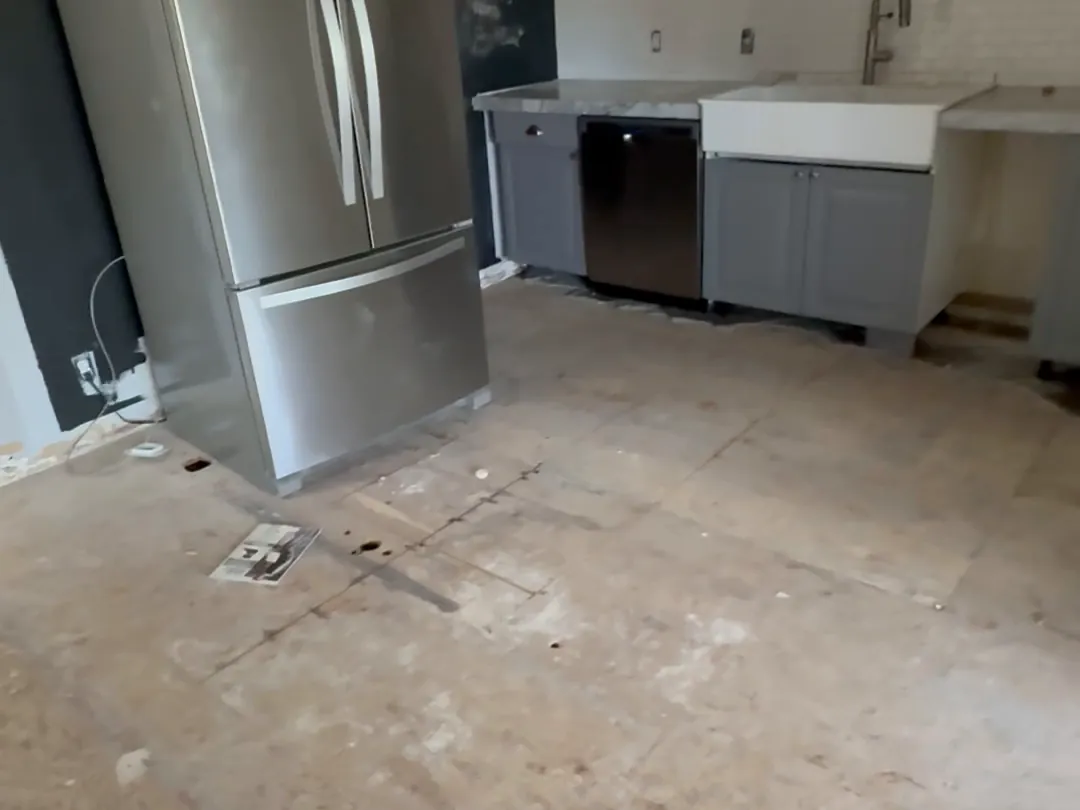 Kitchen with the flooring stripped to the subfloor and the refrigerator pulled out